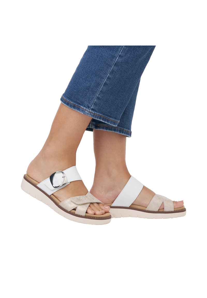 White and tan sandals with cross straps, a round metallic accent, and a textured sole. The design features a cushioned, low-profile construction.