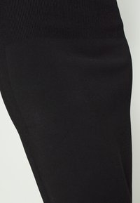 Černá elastická tkanina s hladkým povrchem, s žebrovanými detaily na horním okraji a přiléhavým designem. Žádné viditelné vzory nebo kovové prvky.