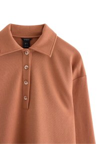 Polo tričko v barvě rzi s jemnou texturou, vybavené límečkem, třemi knoflíky a úzkým střihem.