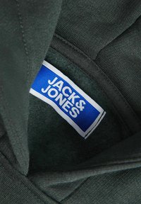 Tessuto verde scuro con una consistenza morbida, caratterizzato da un'etichetta blu con la scritta "JACK & JONES" in bianco, cucita nella zona del colletto.