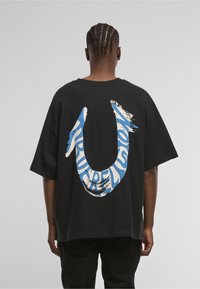 Czarny, oversize'owy t-shirt z dużym niebiesko-białym logo na plecach. Krótkie rękawy, okrągły dekolt i luźny krój.