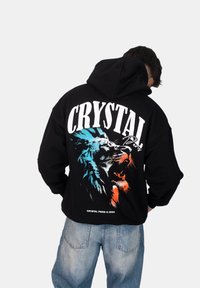 Felpa nera con grafica di un leone colorato e testo "CRYSTAL Paris" sul retro. Vestibilità ampia e tessuto morbido.