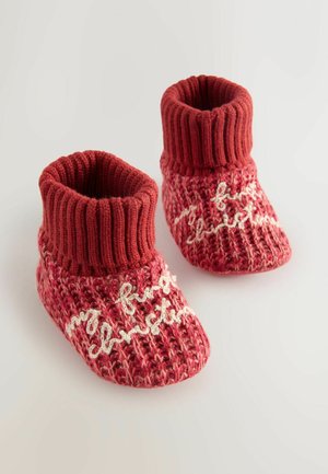 Strickierte rote Baby-Stiefel mit geripptem Bund, versehen mit weißem Text "mein erstes Weihnachten" auf einer strukturierten Oberfläche.