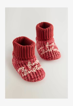 Pletene rdeče otroške škornje z rebrastim robom, ki vsebujejo bel napis "moje prvo božič" na teksturirani površini.