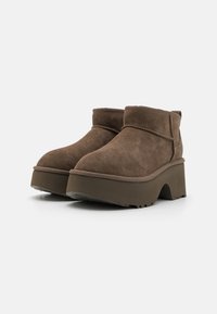 Botas de tobillo de ante marrón con una suela de plataforma gruesa, punta redondeada y un diseño con vueltas. Presenta acentos cosidos y una superficie texturizada.