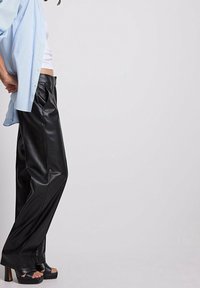 Svarta läderbyxor med vid ben-design, kombinerat med en ljusblå randig skjorta. Outfiten har en avslappnad passform och platåsandaler.