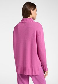 Maglione oversize di colore rosa chiaro, realizzato in un tessuto morbido, con un collo a coste alto e orli a coste. Presenta un piccolo dettaglio del logo sul retro. Maniche lunghe.