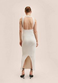 Sukienka maxi dzianinowa w kolorze ecru, z odkrytymi plecami i rozcięciem po boku. Strukturalny materiał prążkowany oraz szerokie ramiączka to wyróżniające się elementy designu.