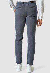 Slim-fit mörkblå byxor med fiskbensmönster, två bakfickor och ren fåll. Bärs med vita sneakers och en vit skjorta.