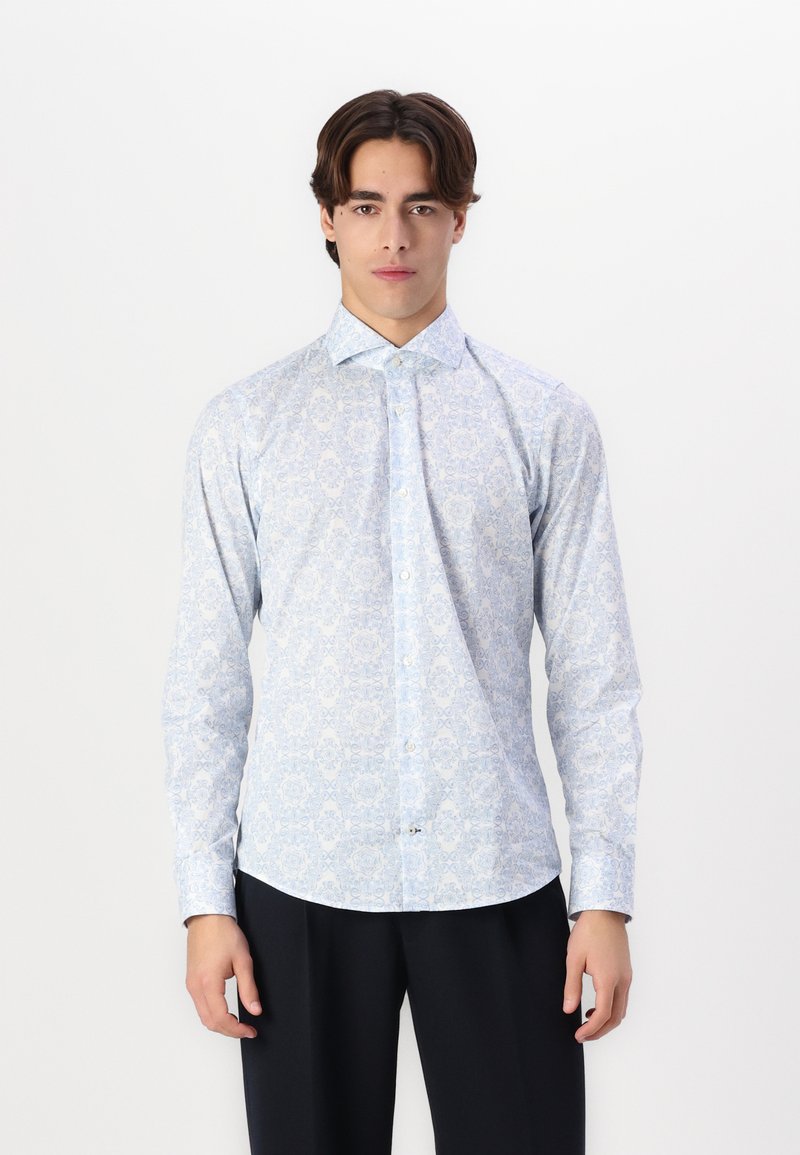 Lichtblauw bloempatronen shirt met een puntige kraag, knoopsluiting en lange mouwen, gemaakt van een gladde stof. Zwarte broek gedragen.