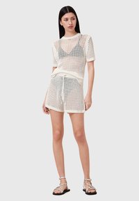Hvid strikket outfit bestående af en kortærmet top og mellemlange shorts. Materialet har et åbent mesh-design med en afslappet pasform.