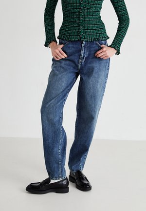 Light blue denim jeans with a relaxed fit, featuring a high waist and subtle faded patches, paired with black loafers.