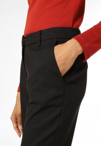 Pantalon noir ajusté avec une texture lisse, doté de poches latérales et d'un devant plat. Assorti avec un haut rouge à manches longues.