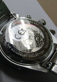 Suds sudraba nerūdīga tērauda pulkstenis ar detalizētu aizmuguri, kurā attēlots globuss, zīmola nosaukums un teksts, kas norāda uz Waterbury kolekciju.