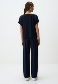 Top blu navy leggero e morbido con maniche arrotolate e pantaloni a gamba larga realizzati in tessuto liscio e morbido; presenta una silhouette rilassata.