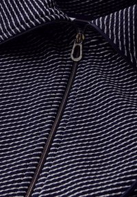 Námořnická pruhovaná zipová bunda s texturovanou tkaninou. Má stříbrný zip a vysoký límec. Pruhy jsou horizontální a rovnoměrně rozložené.