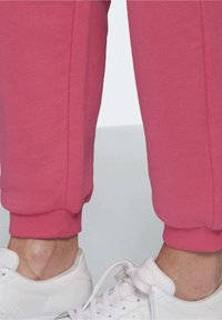 Pantalons de jogging roses avec des poignets élastiques, en tissu doux. Accompagnés de baskets blanches avec une surface texturée et des lacets.