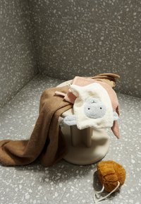 Towels in brown, pink, and cream colors resting on a beige stool; features a fluffy animal face towel and a soft, brown, textured toy.