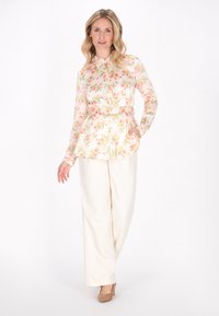 Blomstrete bluse med knaplukning foran, lange ærmer og bælte i taljen, parret med cremede vidde bukser og beige hæle.