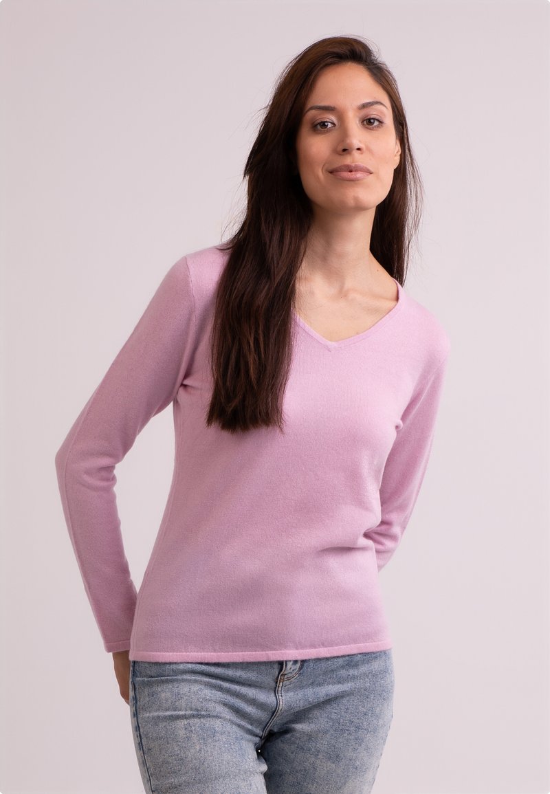 Ljusrosa V-ringad tröja i mjukt material, med långa ärmar och en figurnära passform, tillsammans med blå denimjeans.