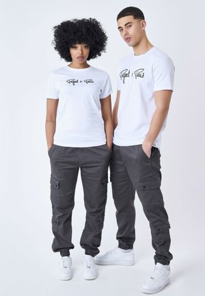 Camisetas blancas con estampado gráfico negro y pantalones cargo grises con múltiples bolsillos, terminados con puños elásticos, combinados con zapatillas blancas.