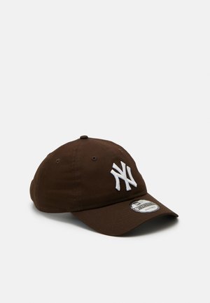 Braune Baseballkappe mit weißem gesticktem "NY"-Logo, gebogenem Schirm, sechs Belüftungslöchern und einem Markenschild am Schirm.