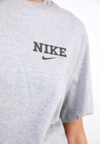 Szara bawełniana koszulka z czarnym logo "NIKE" oraz swooshem. Standardowy okrągły dekolt i krótkie rękawy o gładkiej fakturze.