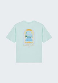 T-shirt bleu clair avec un imprimé au dos d'une vue côté piscine à travers une fenêtre en arc, soleil, palmier, yacht, et le texte « Luxury Life Dreaming of Monaco. »