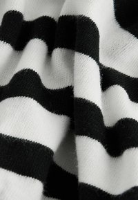Tissu tricoté doux avec de larges rayures horizontales noires et blanches, présenté en gros plan avec une texture et des plis visibles.