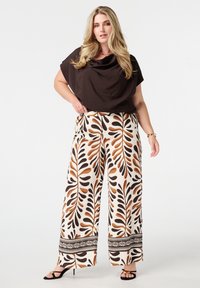 Blouse noire drapée associée à un pantalon large avec une base crème et un grand motif de feuilles brunes et noires, bordé d'une bordure décorative.