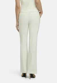 White, flared trousers with a smooth texture and back pockets, paired with black high-heeled shoes in a neutral background.