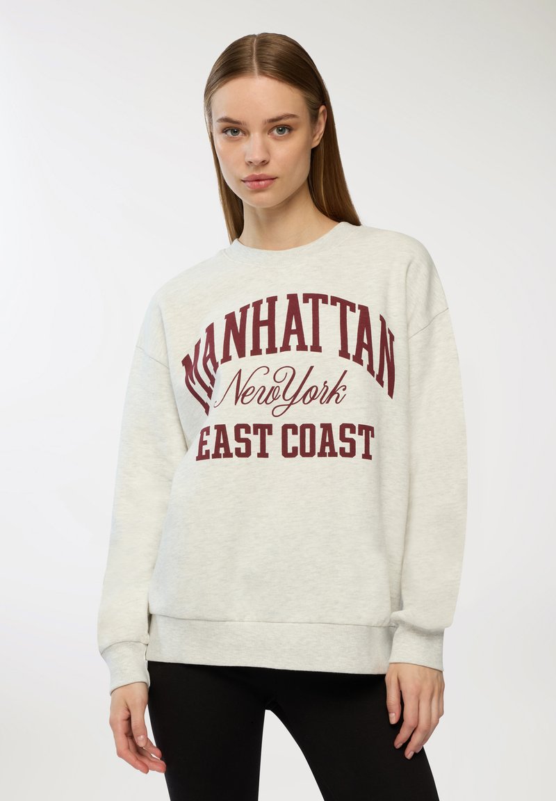Felpa grigia chiara con testo bordeaux che recita "MANHATTAN New York EAST COAST." Presenta un collo a giro e polsini a coste.