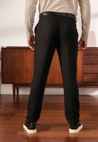 Pantaloni neri con una vestibilità sartoriale, caratterizzati da una striscia lungo il lato. Indossati con una maglia a maniche lunghe a righe e sneakers nere.