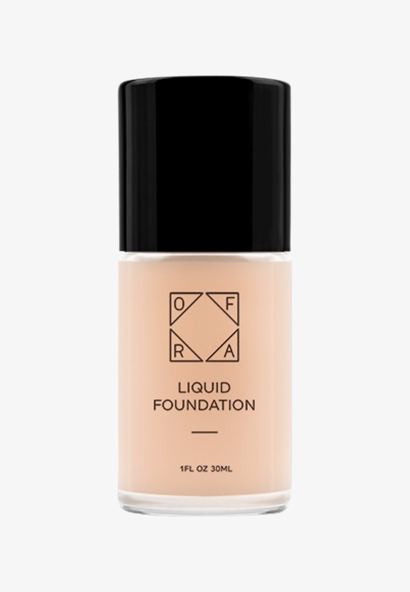 Vloeibare foundation in een transparante glazen fles, beige vloeistof, met een elegante zwarte dop. Het etiket bevat de merknaam en productdetails in zwarte druk.