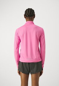 Dlouhý rukáv sportovního topu v živé růžové barvě, vyrobený z hladké, elastické látky; má stojáček a reflexní prvek na zadním okraji.