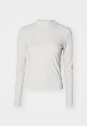 Maglietta a maniche lunghe, grigia chiara a costine con collo alto. Presenta una silhouette aderente e una texture morbida. Nessun motivo o hardware visibile.