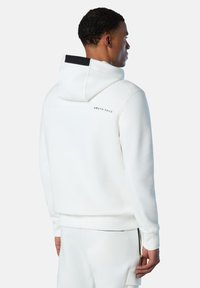 Felpa bianca con logo sul retro, dotata di cappuccio regolabile con cordino, polsini a coste e una texture liscia. Abbinata a pantaloni coordinati.