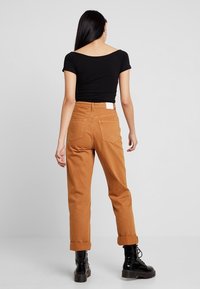 Sort tætsiddende top kombineret med orange-brune bukser med højt talje og opkørte bukseben. Bukserne har to baglommer og et lille hvidt mærke.