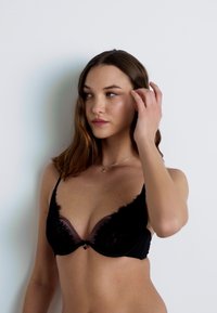 Black lace bra featuring sheer cups, embroidered detailing along edges, adjustable straps, and a small center bow accent.