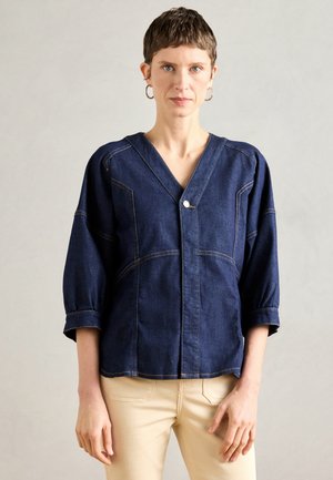 Τζιν μπλούζα με βαθύ V-λαιμό, τρία τέταρτα φουσκωτά μανίκια, μπροστινό κλείσιμο με κουμπιά και αντίθετη κίτρινη ραφή σε σκούρο μπλε ύφασμα.