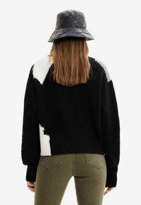 Sweter w kolorach czarno-białych z blokowym wzorem, wykonany z teksturowanego dzianiny, z prążkowanym wykończeniem na dole, szerokimi rękawami oraz kontrastującym dzianym panelem z tyłu.