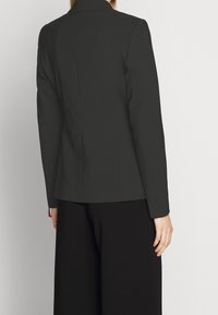 Černý blazer s přiléhavým střihem, klopovými límci a dlouhými rukávy. Disponuje hladkou texturou a jemným detailem v zadním švu.