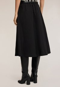 Falda midi negra con cintura elástica, diseño fluido, textura suave, combinada con botas negras de cocodrilo hasta la rodilla.