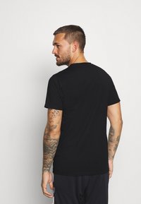 Black cotton t-shirt with a crew neckline, short sleeves, and a fitted silhouette. Features visible tattoos on the arm.