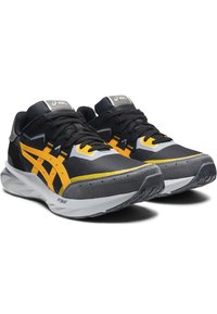 Svarta och gula träningsskor har en slank design, mesh-övre, gummisula och en framträdande Asics-logotyp på tungan. Texturerade detaljer finns.