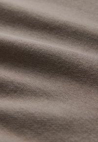 Detailný záber na hladkú, taupe farby látku s viditeľnou jemnou pletenou štruktúrou a mäkkými záhybmi, vytvárajúcimi jemné tiene.