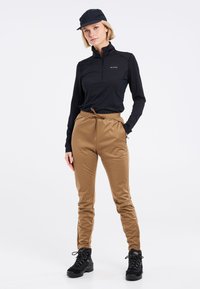 Zwarte langmouw zip-up top, bruine stretchbroek en zwarte veterschoenen. De outfit heeft een sportief ontwerp met een casual pasvorm.