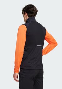 Schwarze und orange Sportweste mit hohem Kragen, ausgestattet mit einem strukturierten Rücken und reflektierenden Akzenten. Das Material ist glatt und eng anliegend.