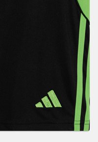 Svart treningsskjorte med grønne kantstriper og en grønn brodert logo nederst til venstre. Laget av et glatt, pustende stoff.