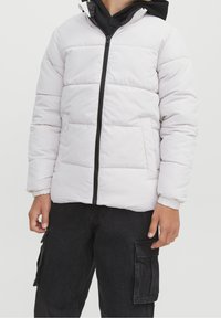 Biała pikowana kurtka z poziomym przeszyciem, czarnym zamkiem błyskawicznym i elastycznymi mankietami. Nosi się ją na czarnej bluzie z kapturem. W zestawie z czarnymi spodniami cargo.